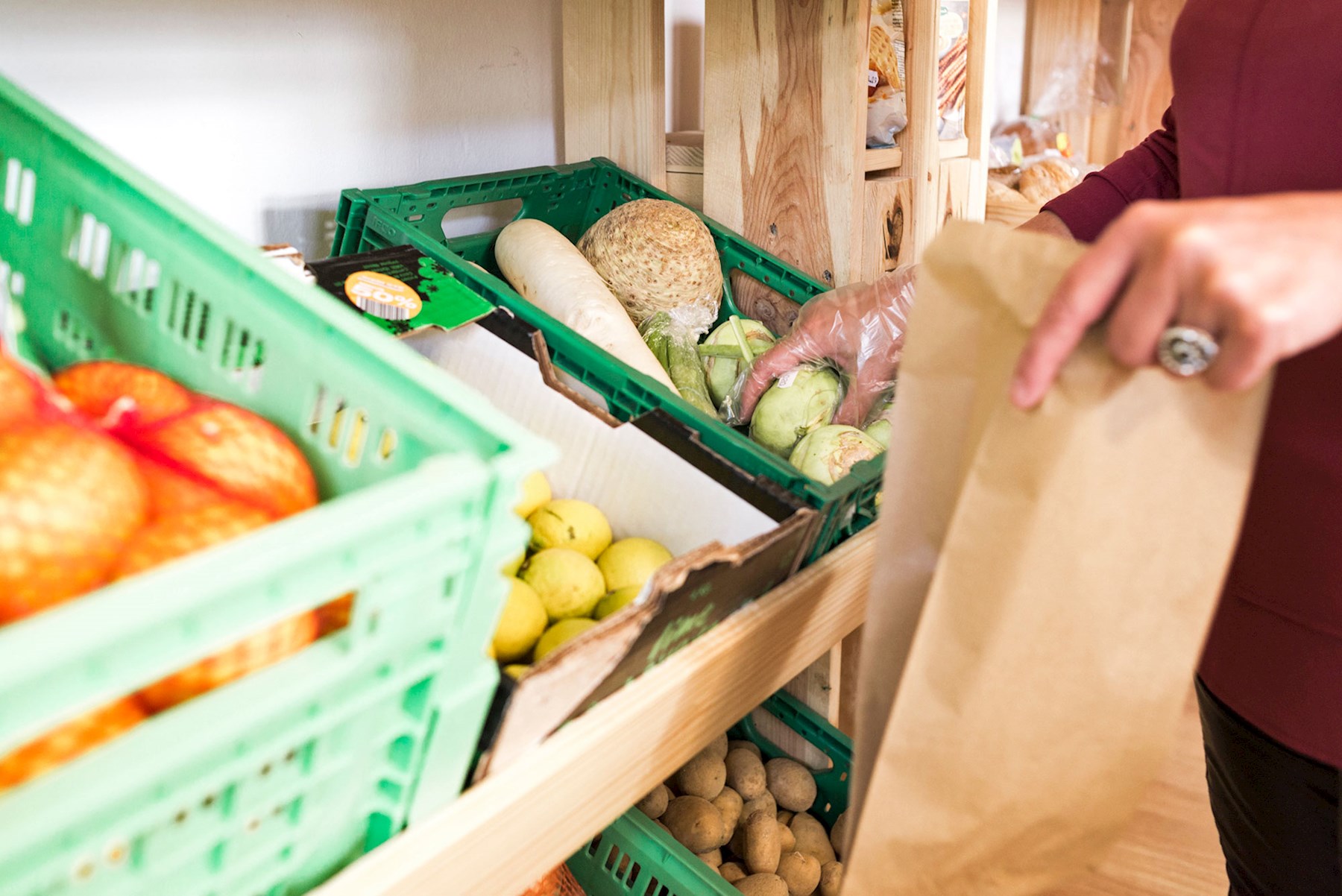 Eine Mitarbeiterin des Sozialmarkts Fürstenfeld mit Einweghandschuh greift nach einem Kohlrabi in der Gemüseabteilung.