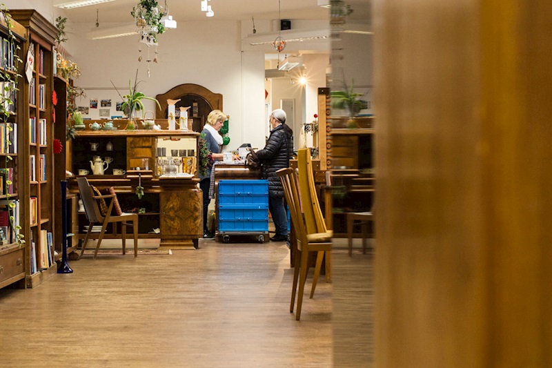 Die Einrichtung des Carla-Ladens Fürstenfeld mit schönen Bücherregalen aus Holz. Im Hintergrund berät eine Mitarbeiterin eine interessierte Kundin.